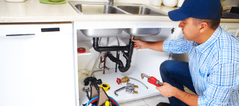 a professional plumber in Franklin, PA providing repairs to kitchen sink pipes underneath a kitchen sink