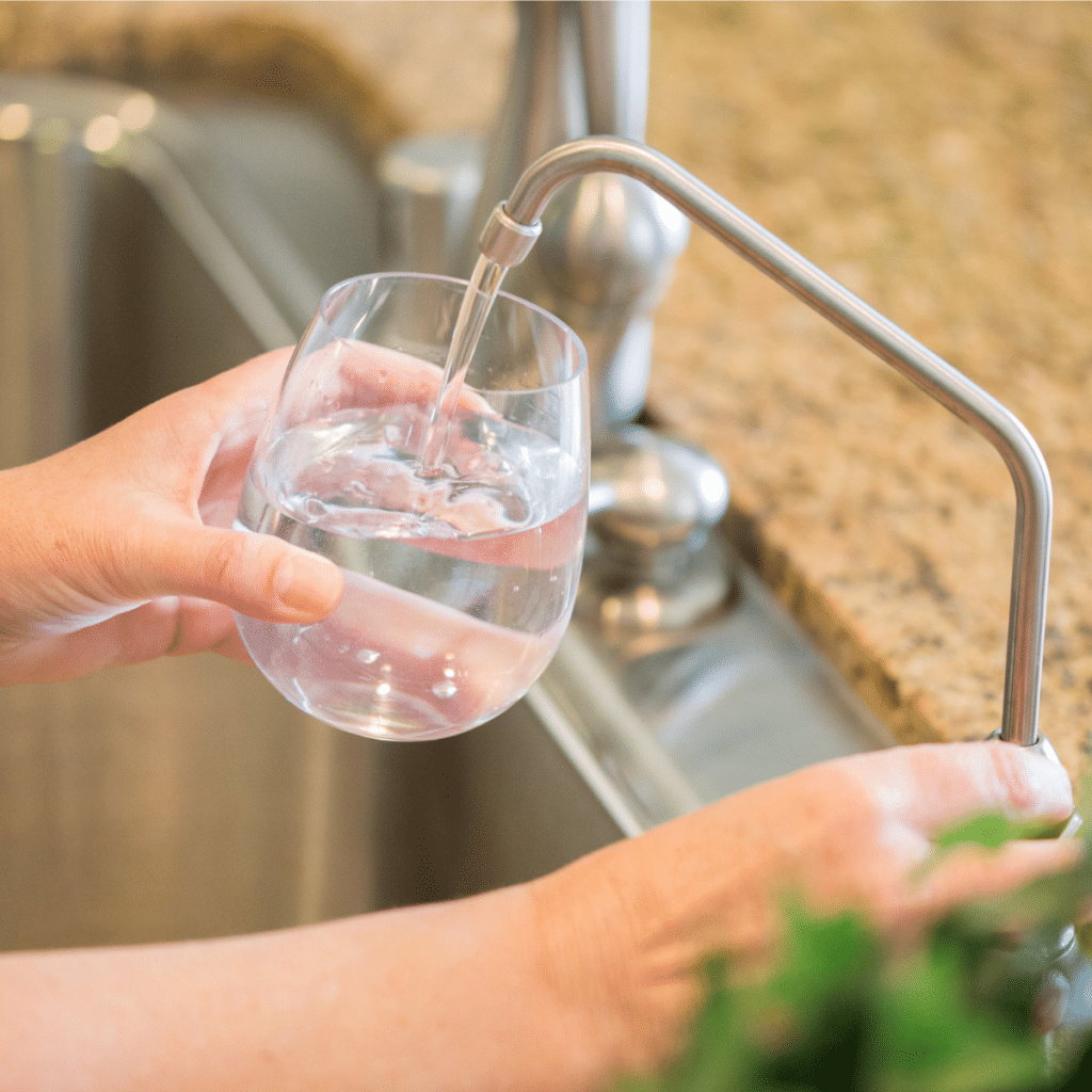 hands of a woman turning on a kitchen water faucet to fill a glass