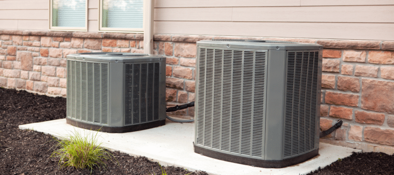 two outdoor HVAC units on a concrete slab next to a home