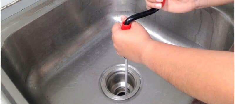 technician hands using a drain snake and putting it down a kitchen sink to clear the drain